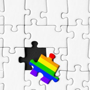 One piece painted in colors of rainbow is lies separately. Background from stacked gray white puzzles. Concept of equality and acceptance of sexual minorities lesbian, gay, bisexual, and transgender.